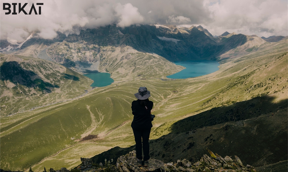 A female trekker standing on the ridge of a mountain looking towards a lake in mountains 