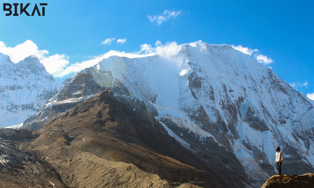 A trekker standing on a rock with a snow capped mountain in background.